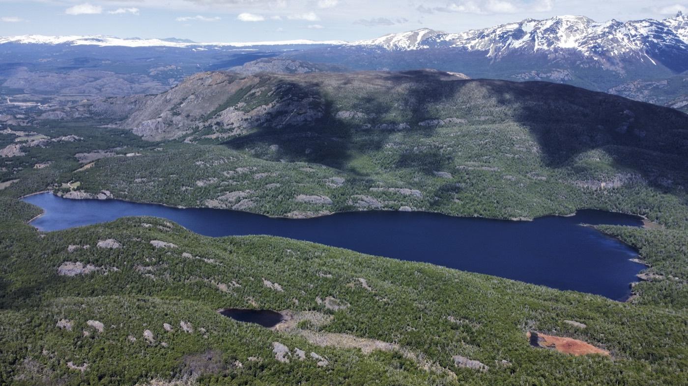 Vista aérea de un lago azul rodeado de bosque nativo y montañas nevadas en Aysén