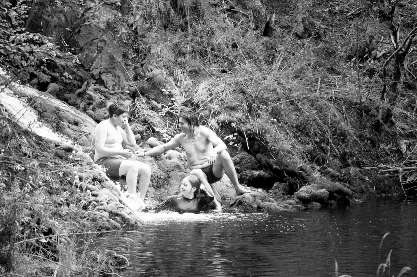 Estudiantes se bañan en una poza del río entre los árboles, en blanco y negro